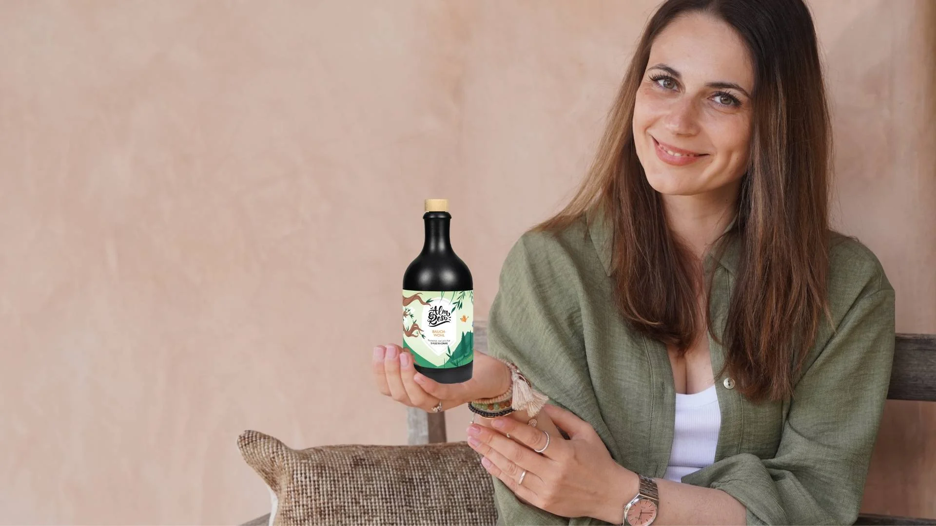 Laechelnde Frau haelt eine Flasche Alm Resi Sauerhonig in den Haenden.
